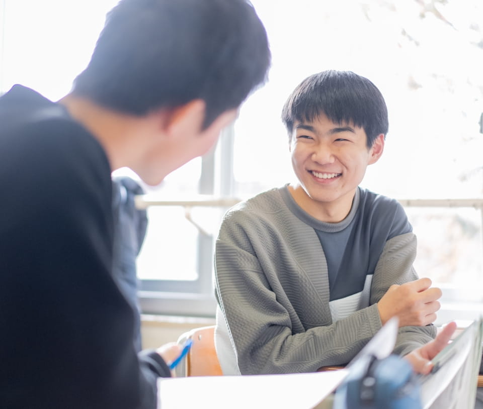 明るい教室で、笑顔で会話を楽しむ2人の学生